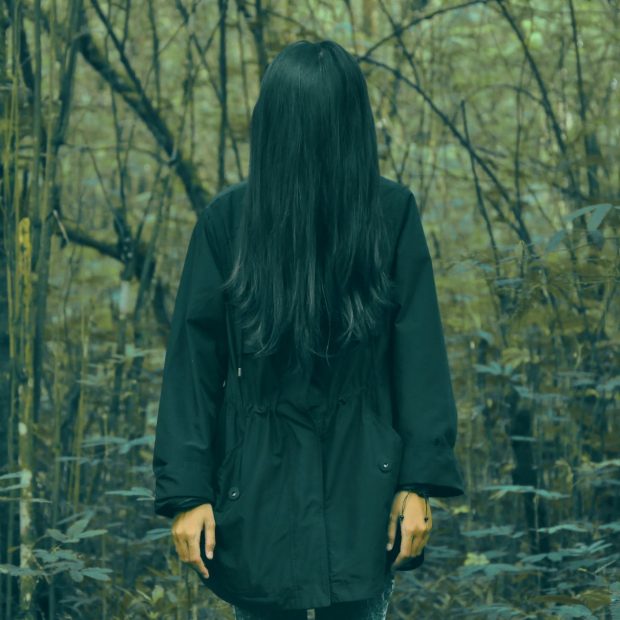 person in black coat standing in forest